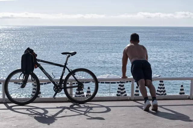 Ein Mann mit nacktem Oberkörper macht am Strand von Nizza neben seinem Fahrrad Übungen. | Foto: Serge Haouzi/XinHua/dpa (Archivbild)