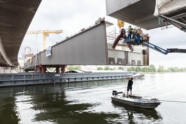 Lückenschluss über dem Main-Donau-Kanal: Am Dienstag, 30. Juni 2026, hat das Projekt Hafenbrücken eine weitere Hürde genommen. Mithilfe zweier Spezialhebegeräte wurde ein 75 Meter langes und 520 Tonnen schweres Brückenteil von zwei Lastschiffen aus in die vorgesehene Lücke gehoben.
 | Foto: Christian Höhn / Stadt Nürnberg