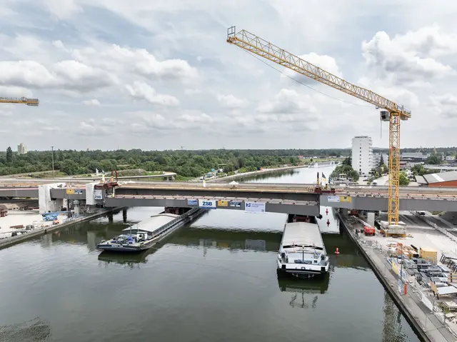Lückenschluss über dem Main-Donau-Kanal: Am Dienstag, 30. Juni 2026, hat das Projekt Hafenbrücken eine weitere Hürde genommen. Mithilfe zweier Spezialhebegeräte wurde ein 75 Meter langes und 520 Tonnen schweres Brückenteil aus Stahl auf zwei Lastschiffen zentimetergenau unter der Brückenlücke positioniert .
 | Foto: Christian Höhn / Stadt Nürnberg