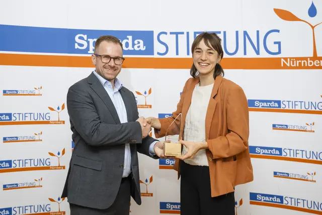 Carolin Hasenauer (r.) gewinnt den SpardaMedienpreis 2026. Zusammen mit ihrer Kollegin Mona Böhm realisierte sie die Reportage „Freiwillig ins Feuer: Die Helden der Feuerwehrschule“ für BR24 Mainfranken. Tobias Rieck (l.), Vorsitzender des Stiftungsvorstands der Sparda-Stiftung Nürnberg, übergab den SpardaMedienpreis 2026. | Foto: Uwe Niklas