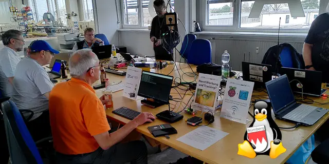 An einem Tisch sitzen mehrere Personen und arbeiten an einigen Notebooks.
